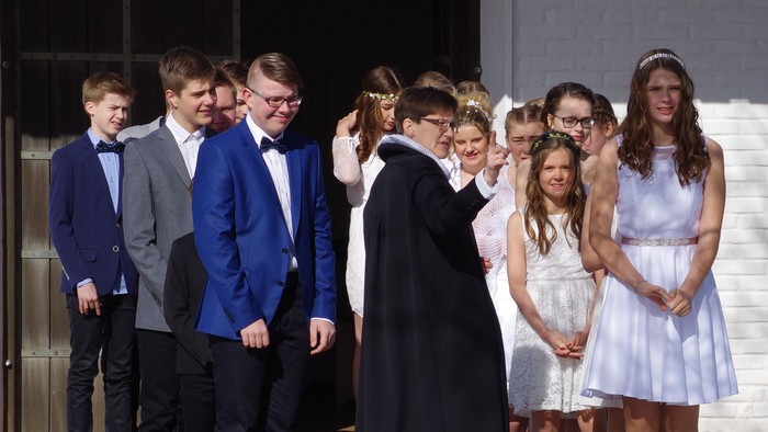 En gruppe ungdomme og unge står i en kreds, nogle i formelt tøj, mens en person i sort klæder står i midten.