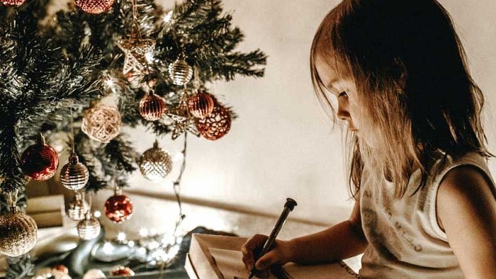 Ein Mädchen schreibt in einem Buch neben einem Weihnachtsbaum.