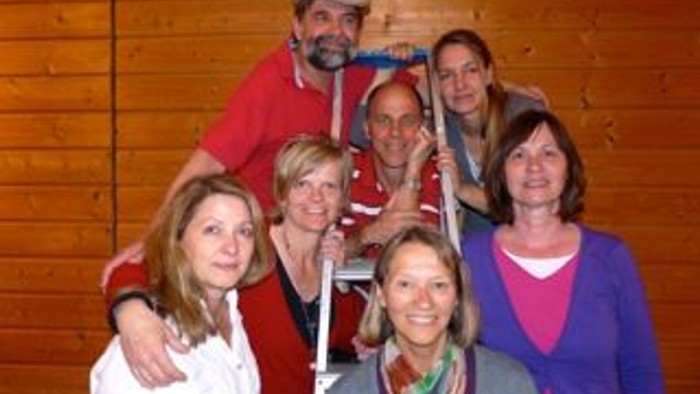 Eine Gruppe von sieben Personen posiert vor einer Holzwand