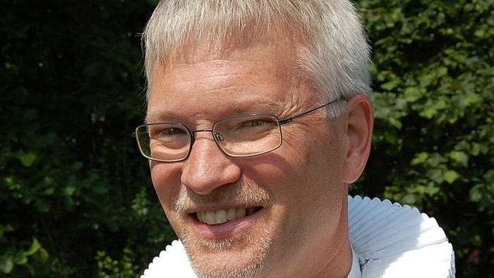 Mand med hvid krage og briller.