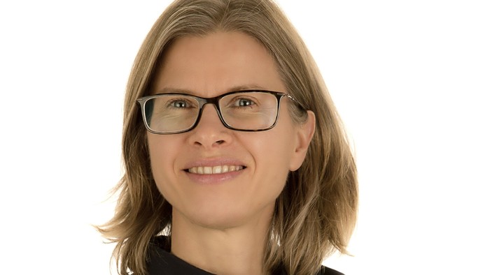 En kvinde med kort, blond hår og briller smiler til kameraet.