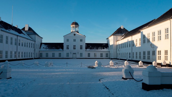 En snedækket gård med tre store hvide bygninger og en klokketårn i midten