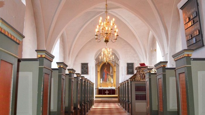 Kirkeinteriør med kirkebænke og lysekrone.