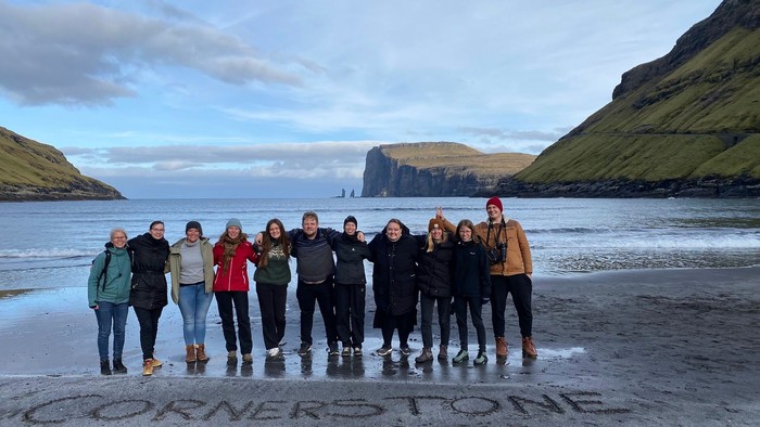 En gruppe af mennesker står sammen på en strand med et bjerg i baggrunden