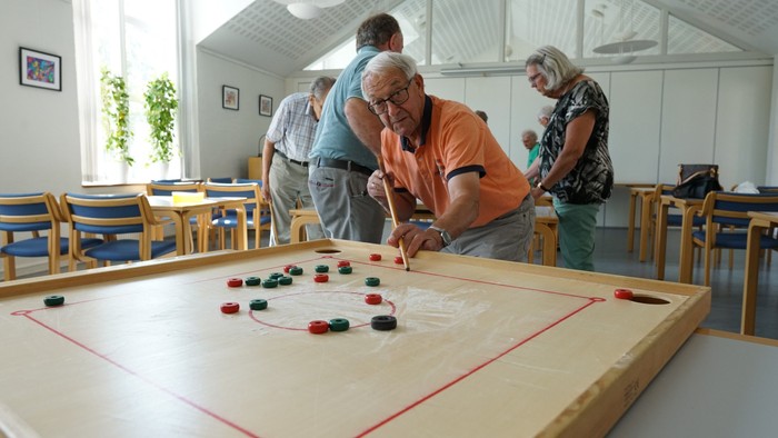 En gruppe ældre folk spiller carrom i et lys og rummeligt rum