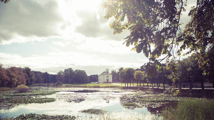 En rolig sø med træer og en hvid bygning i baggrunden
