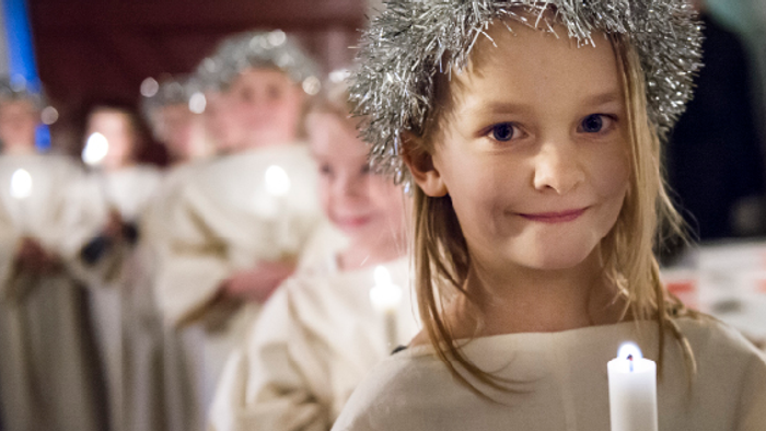 En lille pige med glitrende krone og lyset i hånden.
