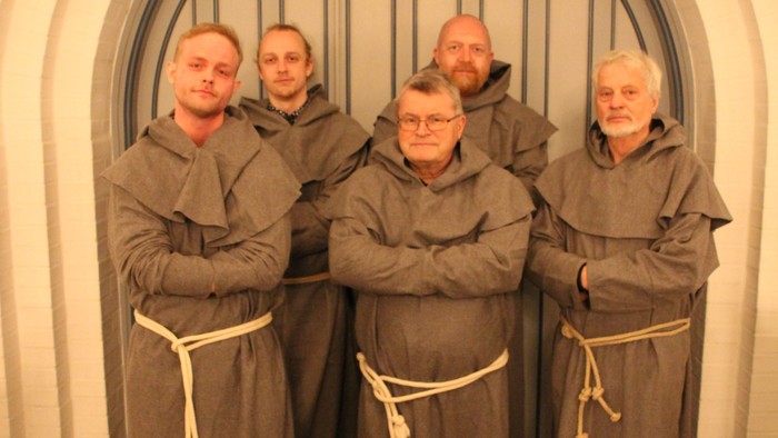 En gruppe mænd i munkedrakter står sammen foran en stor dør.