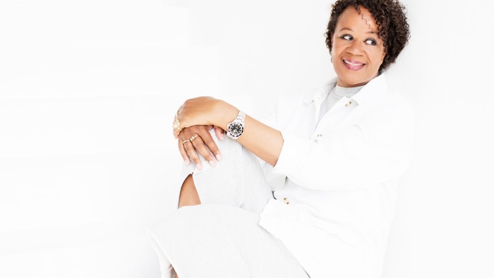 En kvinde i hvid kjole og armbåndur, smiler og ser på sin armbåndur.