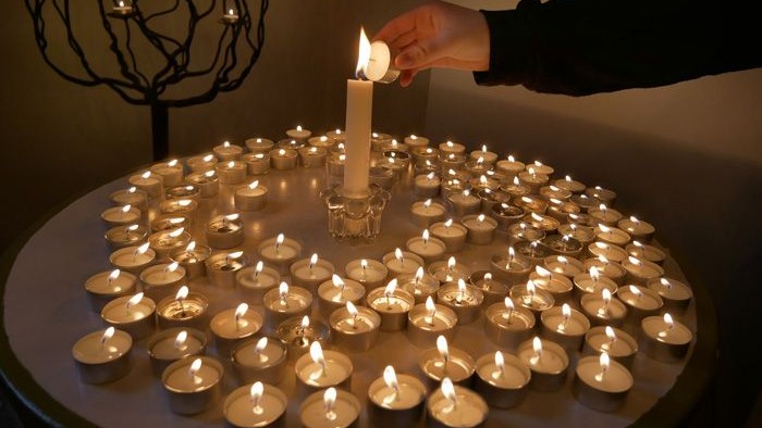 En hånd tænder en lille lysstake i en kreds af andre lysstake.