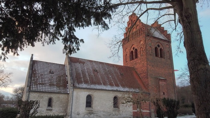 En snedækket kirke med tårn i sneløs landskab