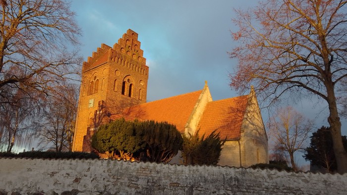 En gammel kirke med teglmur og spisse tårn, belyset af blålys mod en mørk himmel