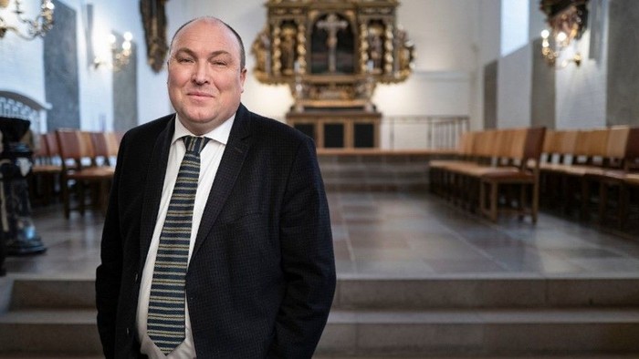 Mand i mørkt kostume og hvid krage står i kirke.