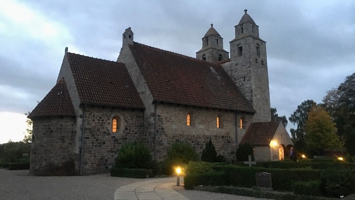 En middelalderlig kirke med spåntak og to tårne ved skumringsbelysning.