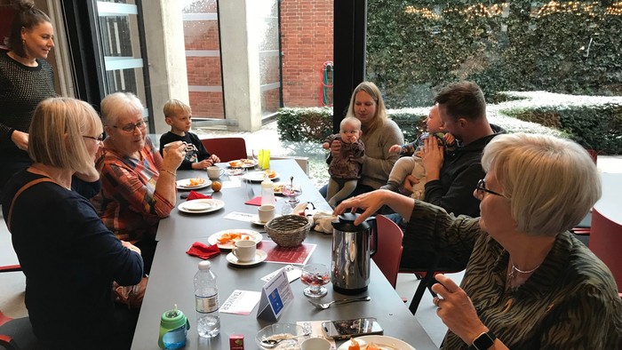 En gruppe af mennesker sidder ved et bord og spiser morgenmad.