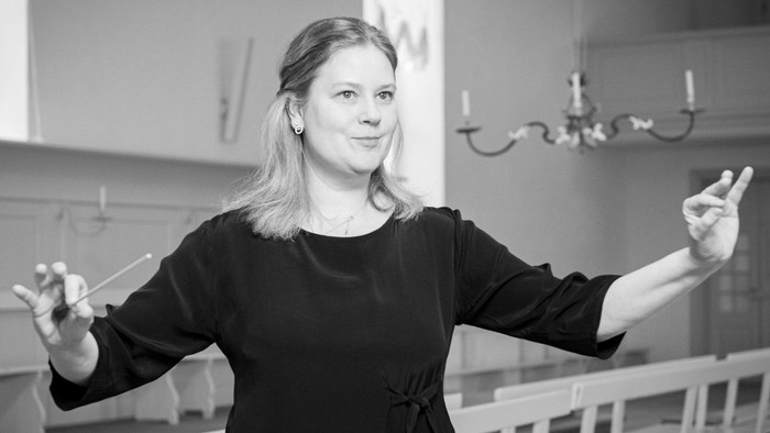 En kvinde dirigerer et orkester i en koncertsal.