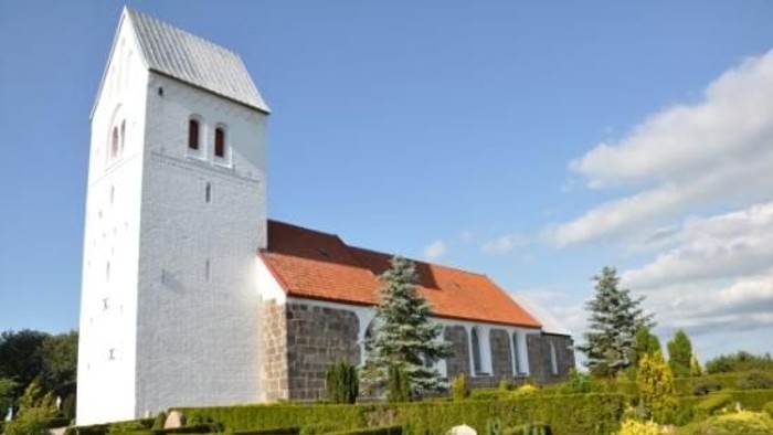 En hvid kirke med tårn og rødt tag i en grøn og træfattig omgivelse