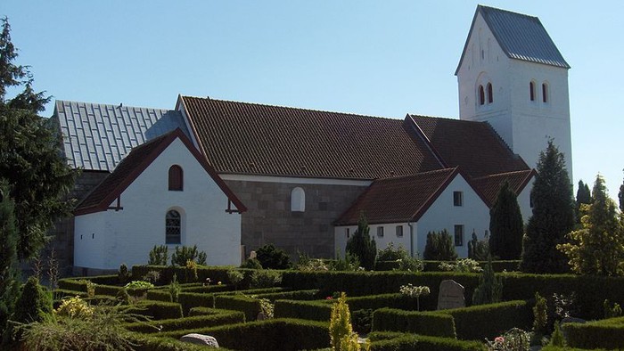 Et hvidt kirkebygningskompleks med tårn og omgivet af en have