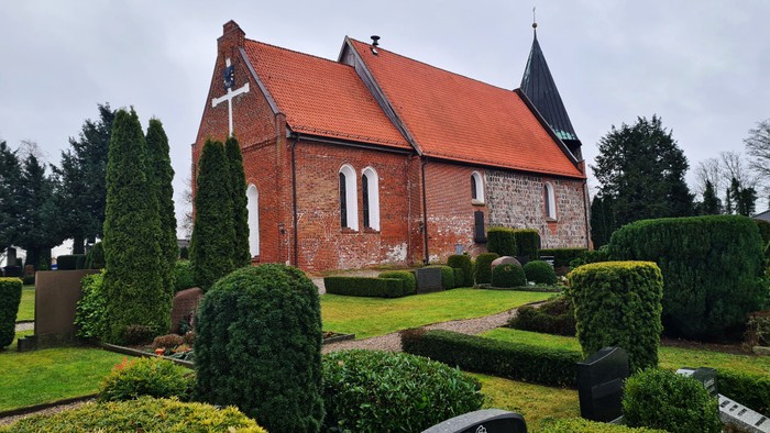Kirchhof mit rotem Backsteingebäude und gut gepflegtem Grün.