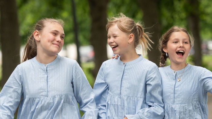 Tre piger løber glade i blå kjoler gennem en park