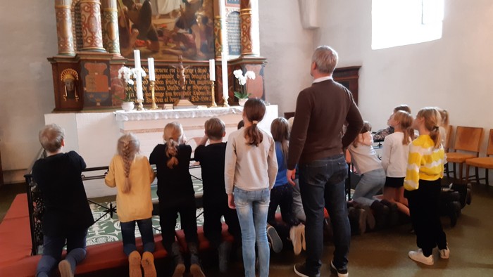 En gruppe børn og en mand står i en kirke og ser opad mod alteret.