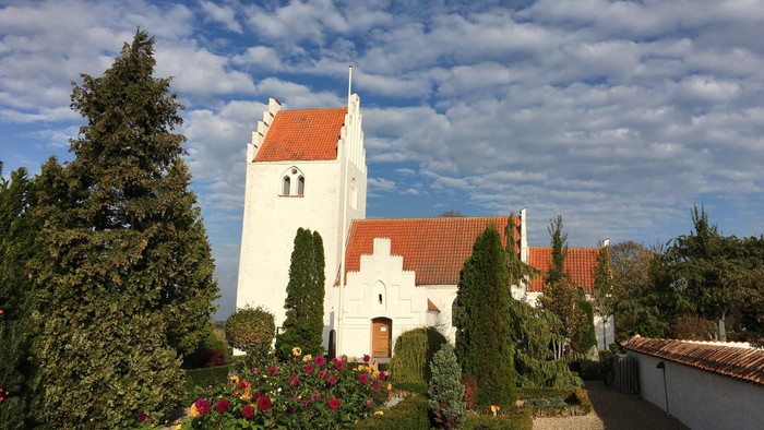 En hvid kirke med rødt tag og en have med blomster og buske