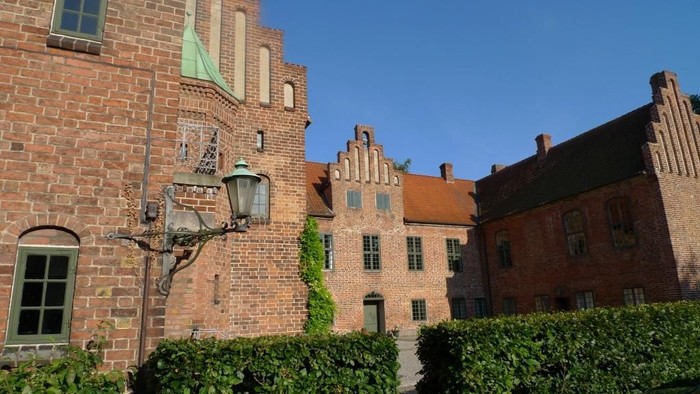 Gamle murstensbygninger med grønne vinduer og en lysblå himmel.