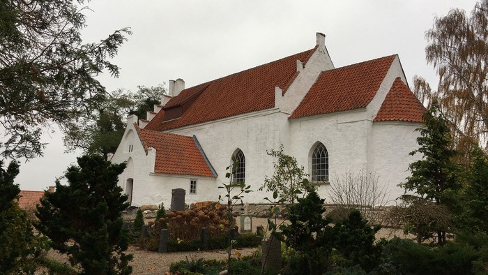 Hvidkalket kirke med rødt tag og kirkegårdens træer og buske 
