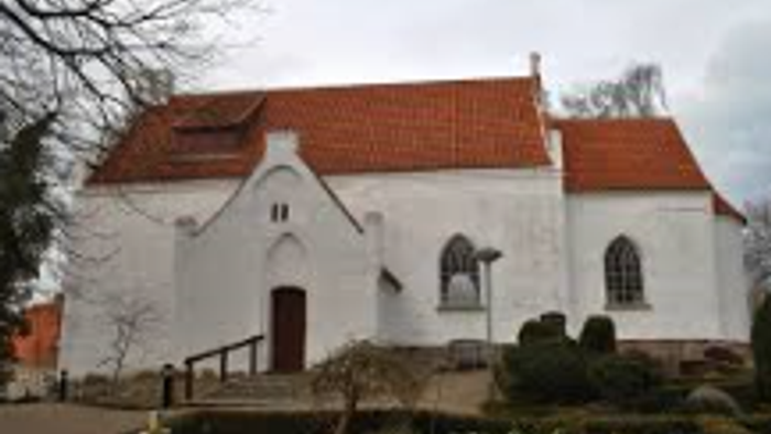 En hvid kirke med rødt tag og en kirkegård.