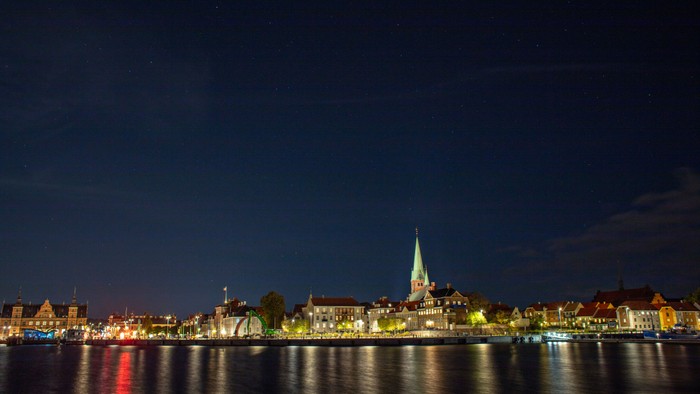 En by ved natt med lysende bygninger og en kirke med spire.