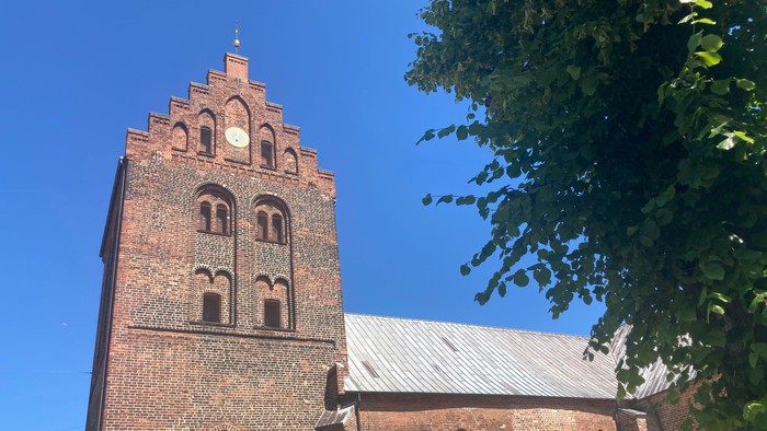 Røde murstenskirke med tårn og spids tak.