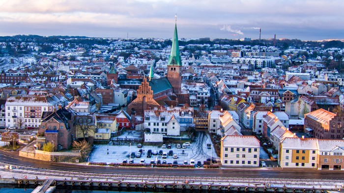Byen med kirke med grøn spire og farvede boliger ved havnen