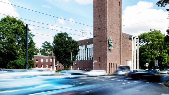 Ein hohes Ziegelgebäude mit Uhrturm an einer belebten Straße