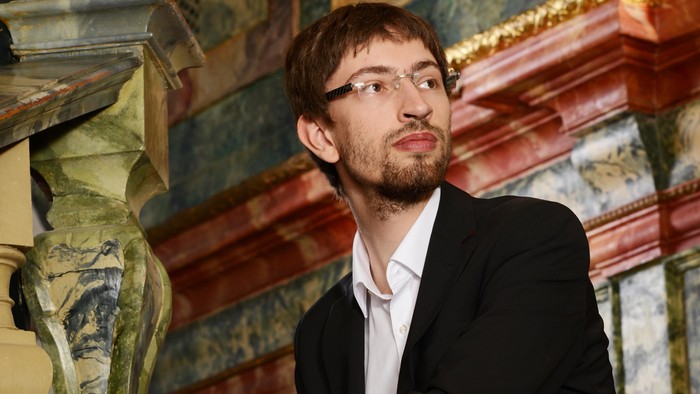 Mann im Anzug sitzt auf Bank vor verziertem Hintergrund