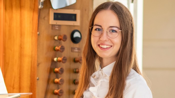 Junges Mädchen sitzt vor einem weißen Klavier und lächelt.