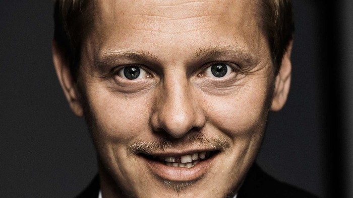 En smilende mand med kort hår og mælkebarte.