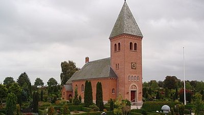 En rød kirke med højt tårn og en have med blomster.