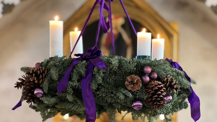 En julekrans med lys og pynt med violette bænder hænger i en lysende indgang