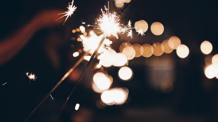 En hånd holder en sparkler i mørket med lysblomster i baggrunden