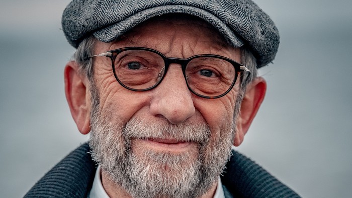 En smukk, eldre mand med briller og baret, der smiler til kameraet.