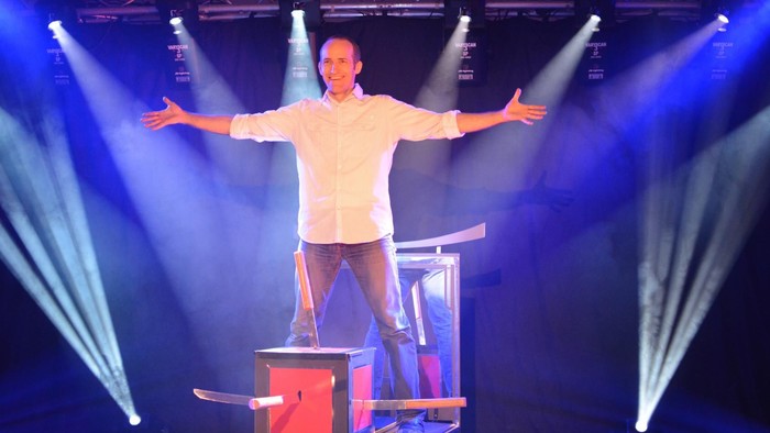 Ein Mann steht auf einem Stuhl, der auf einem Tisch steht, mit ausgebreiteten Armen.