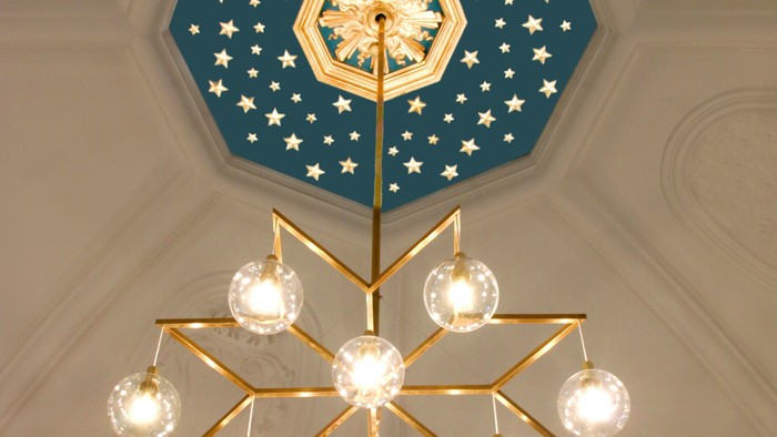 En stor belysning med glasskyer hænger fra et blå tak med stjerner og en midterstjerne.