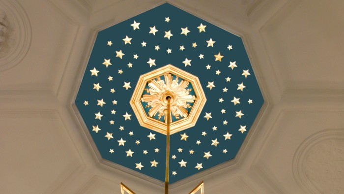 En stor belysning med glasskyer hænger fra et blå tak med stjerner og en midterstjerne.