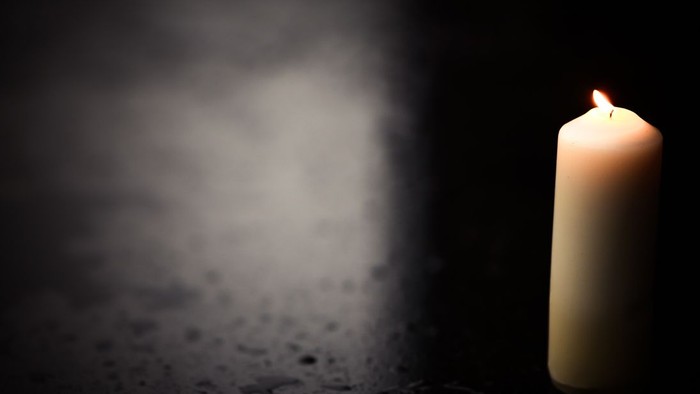 Ein einzelnes, brennendes Kerzenlicht in der Dunkelheit.