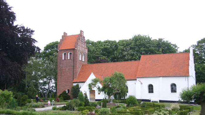 En hvid kirke med røde tag og tårn i en træket garden