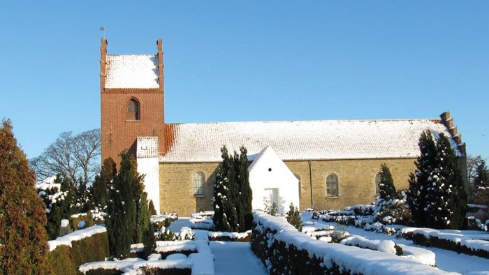 En snede kirke med tårn og hvide vinduer, omgivet af sne og træer
