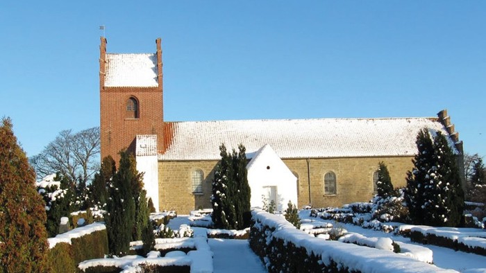 En snede kirke med tårn og hvide vinduer, omgivet af sne og træer