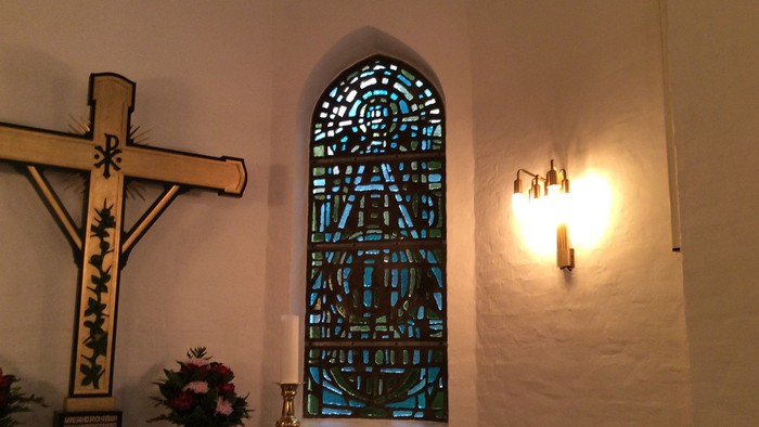 En kirkeindretning med kors, lysestage og glasmaleri
