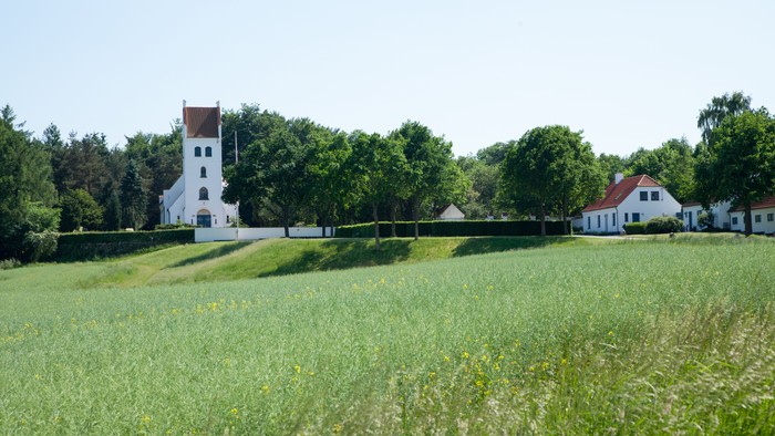 En grøn åben mark med et hvidt tårn og huse i baggrunden