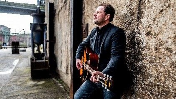 Ein Mann sitzt an einer Steinmauer und spielt Gitarre.